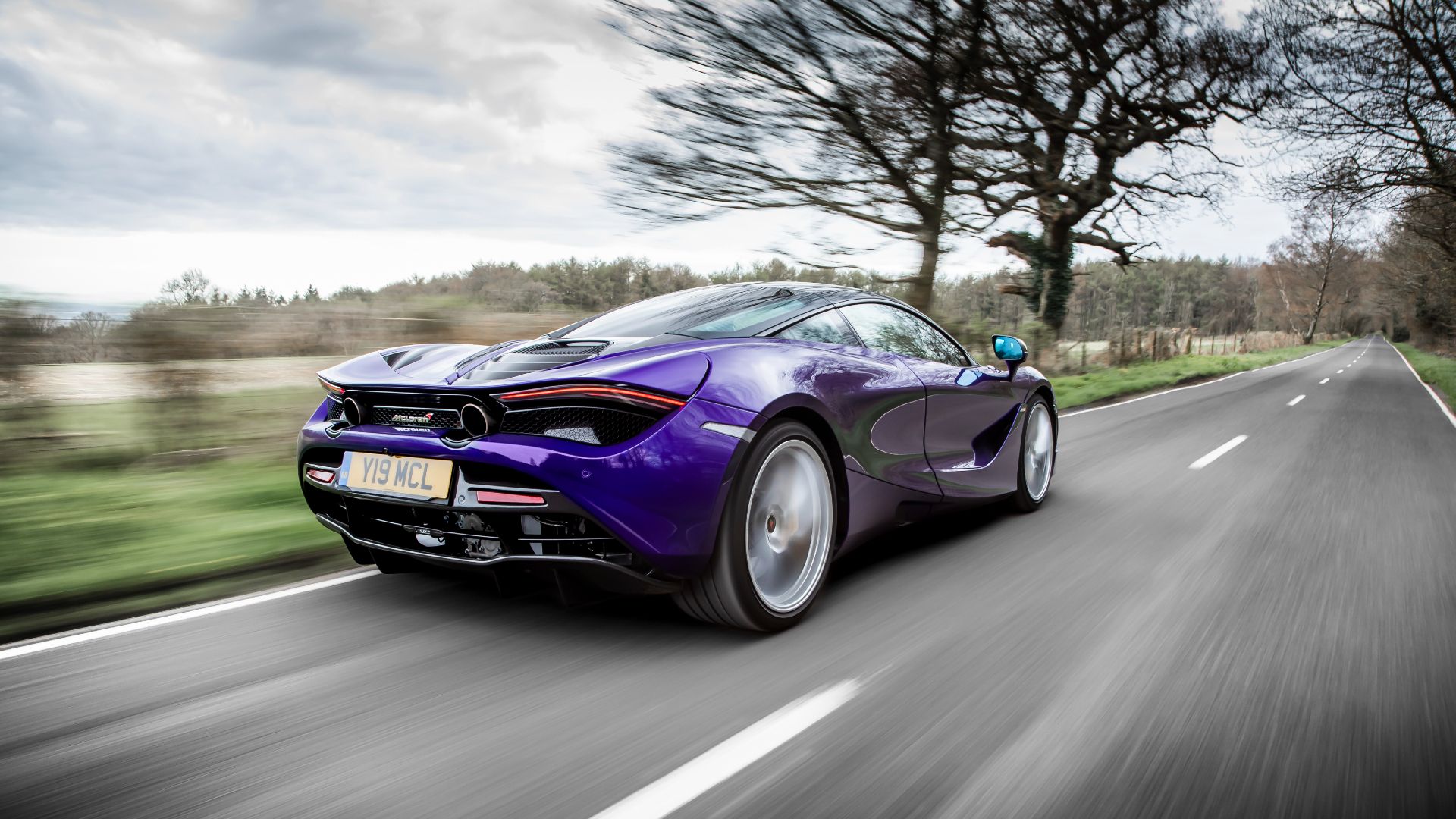 A rear 3/4 action shot of a blue McLaren 720S driving on the road