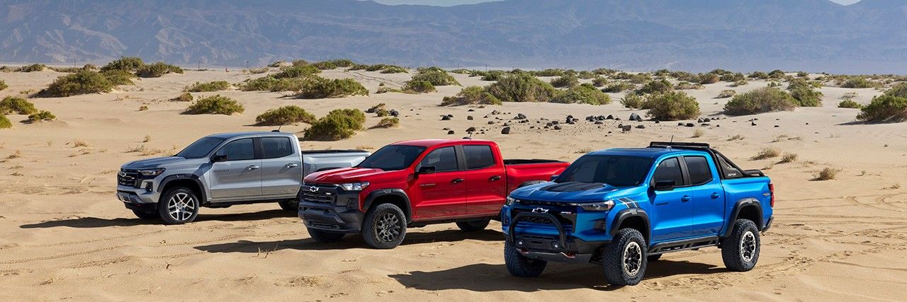 A silver, red, and blue Chevy Colorado trucks parked on sand.