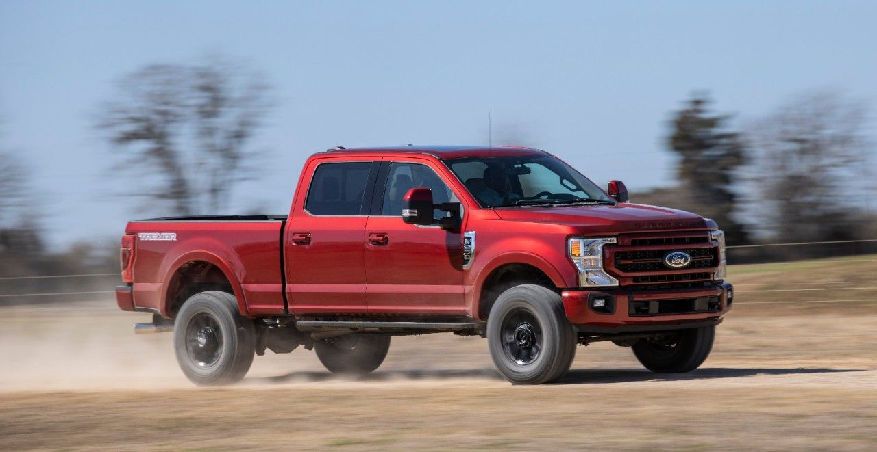 Front three-quarter action shot of a red Ford Super Duty pickup truck driving down a dusty road.