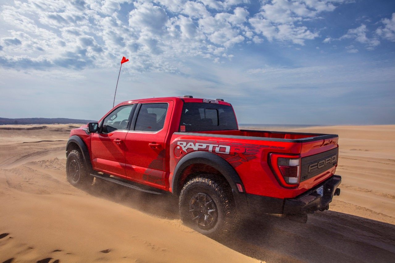Rear three quarters action shot of a red 2023 Ford F-150 Raptor R driving through the desert. 
