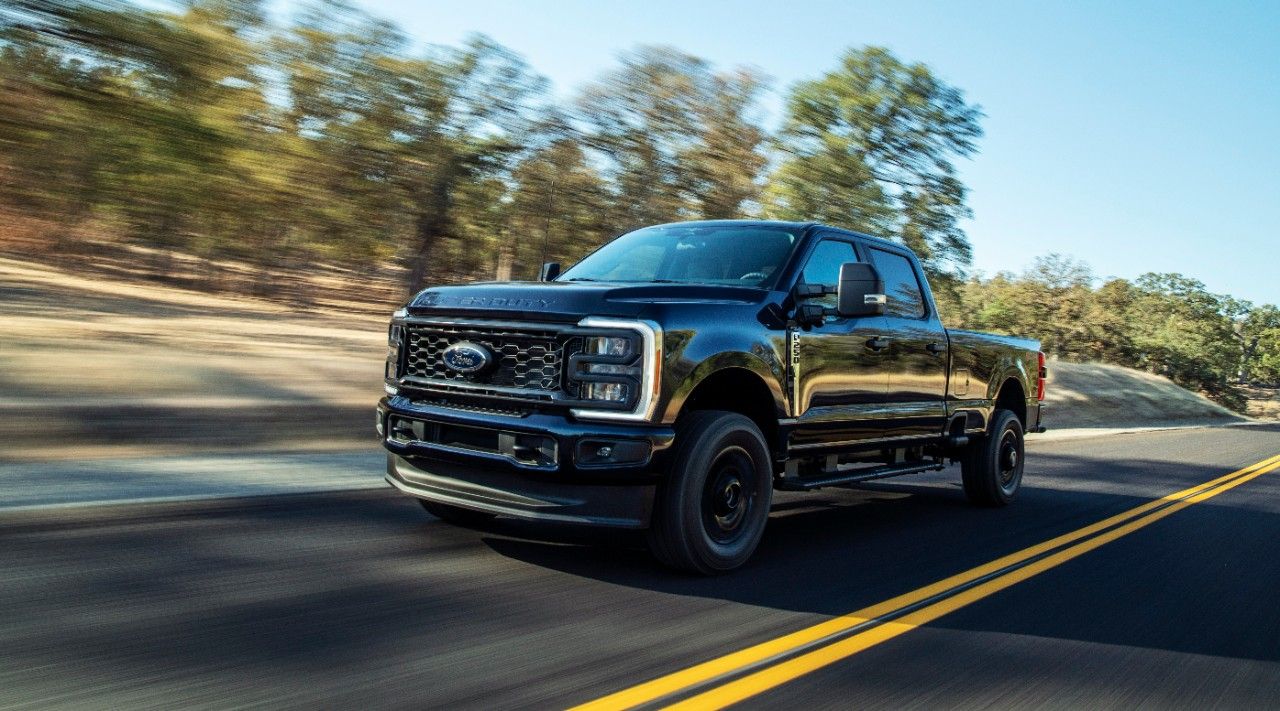 A front three-quarters action shot of a black Ford F-250 Super Duty driving down a road.