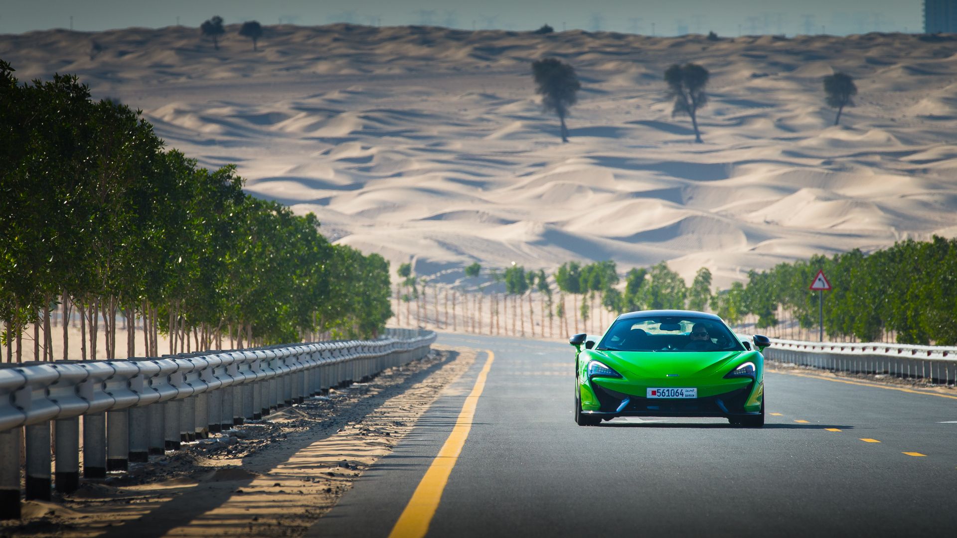 A front shot of a green McLaren 570S driving on the road