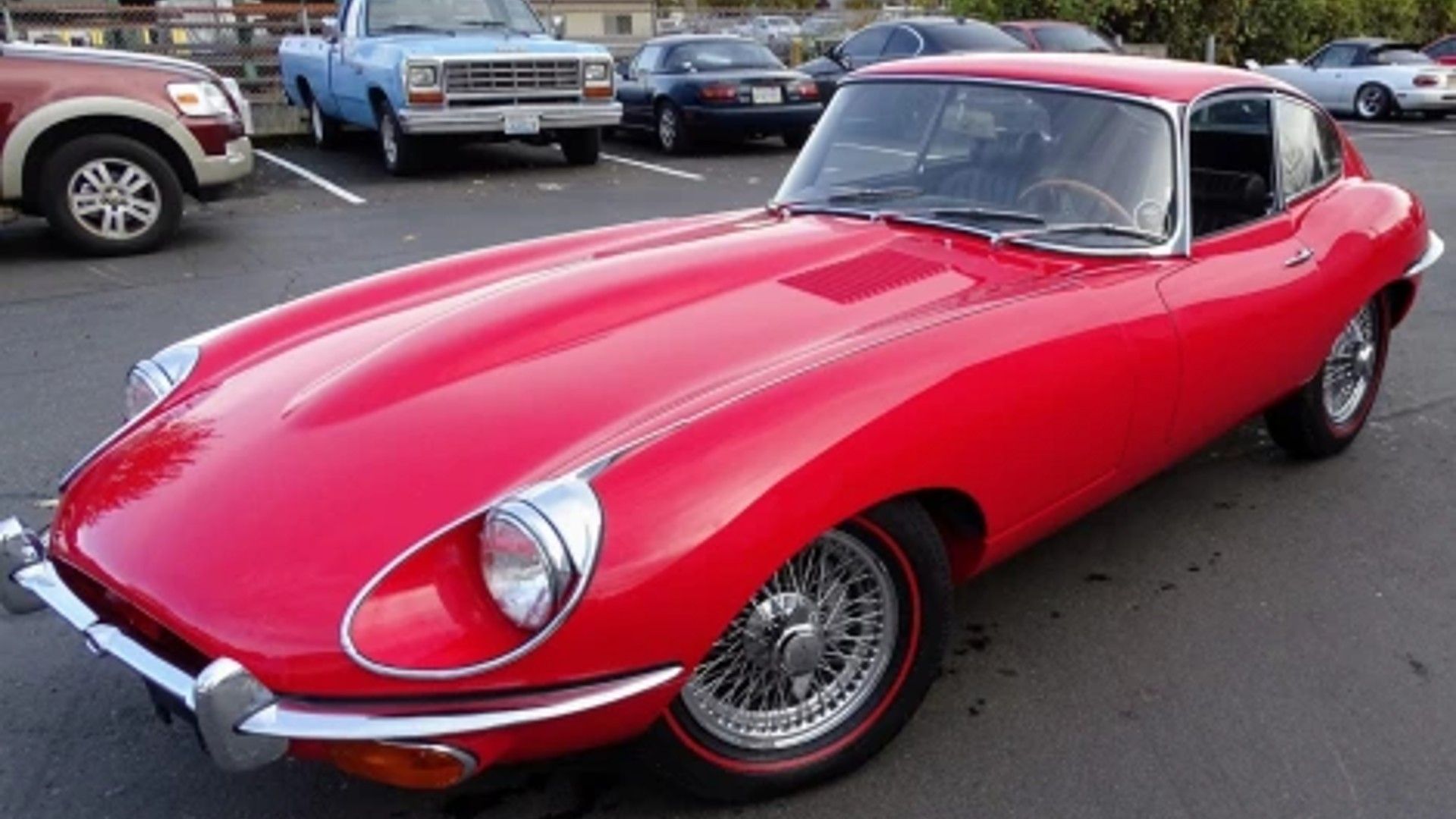 Driver's side profile of a red Jaguar E-Type Coupe.