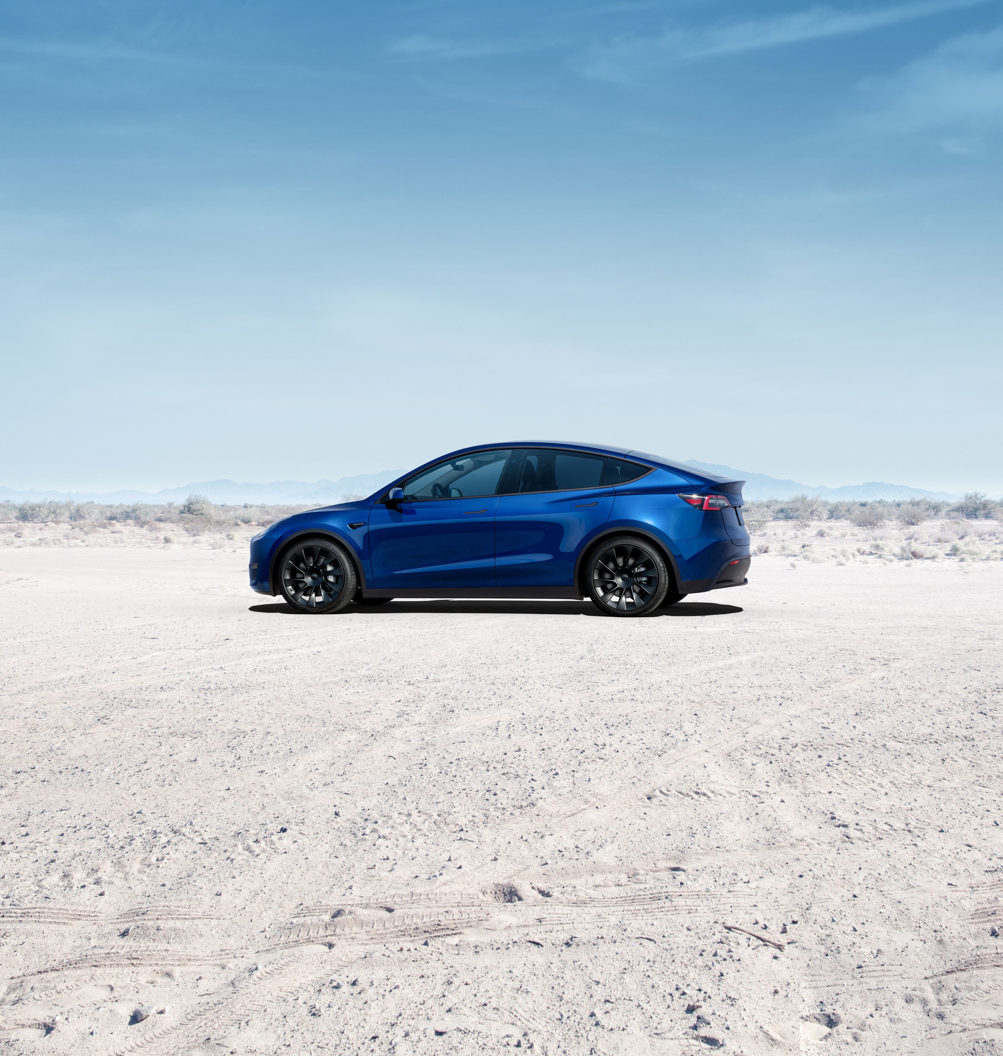 A blue Tesla Model Y parked on the sand.
