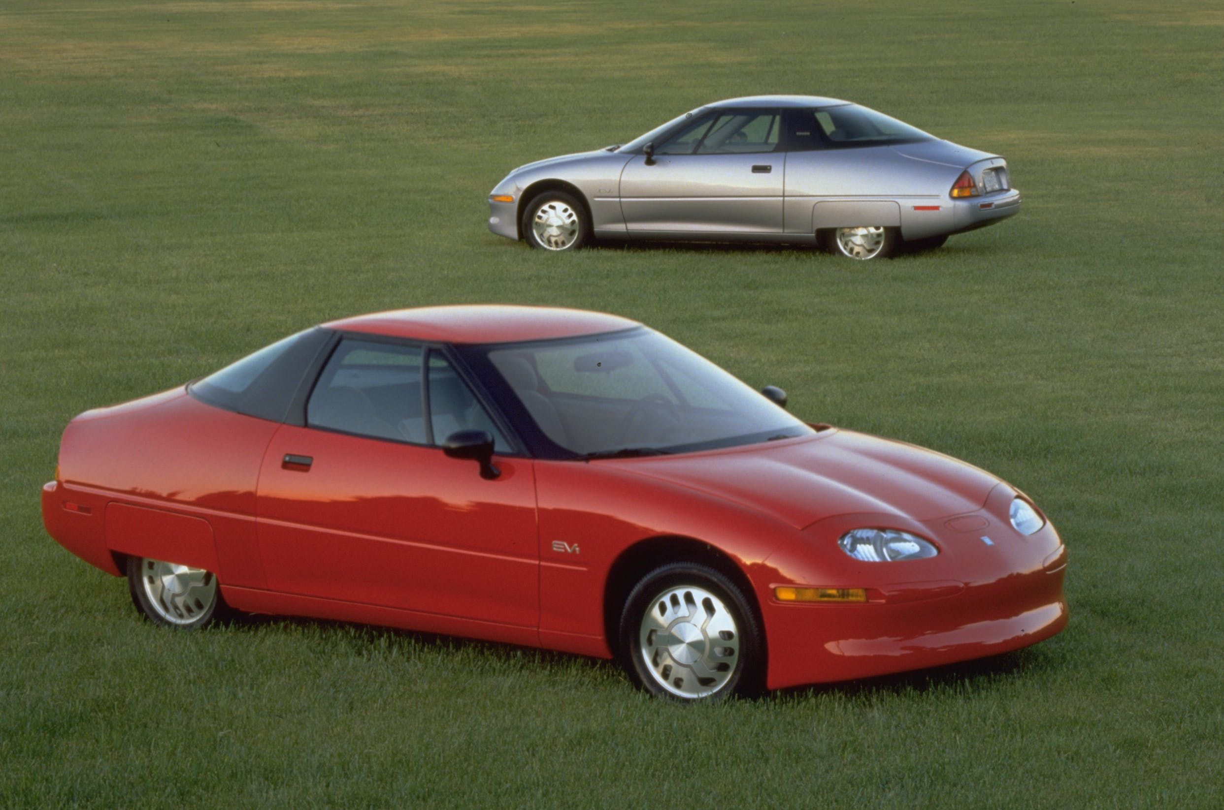Red and silver GM Ev1 cars parked in a grassy field.
