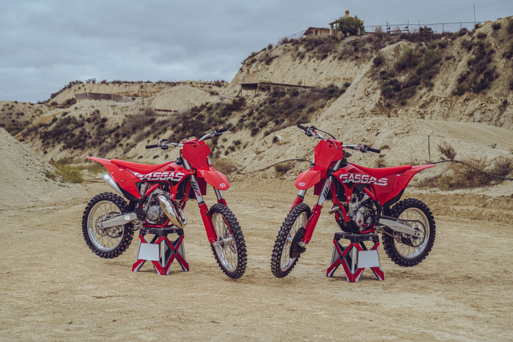 Dua sepeda motor trail merah melawan bukit pasir.