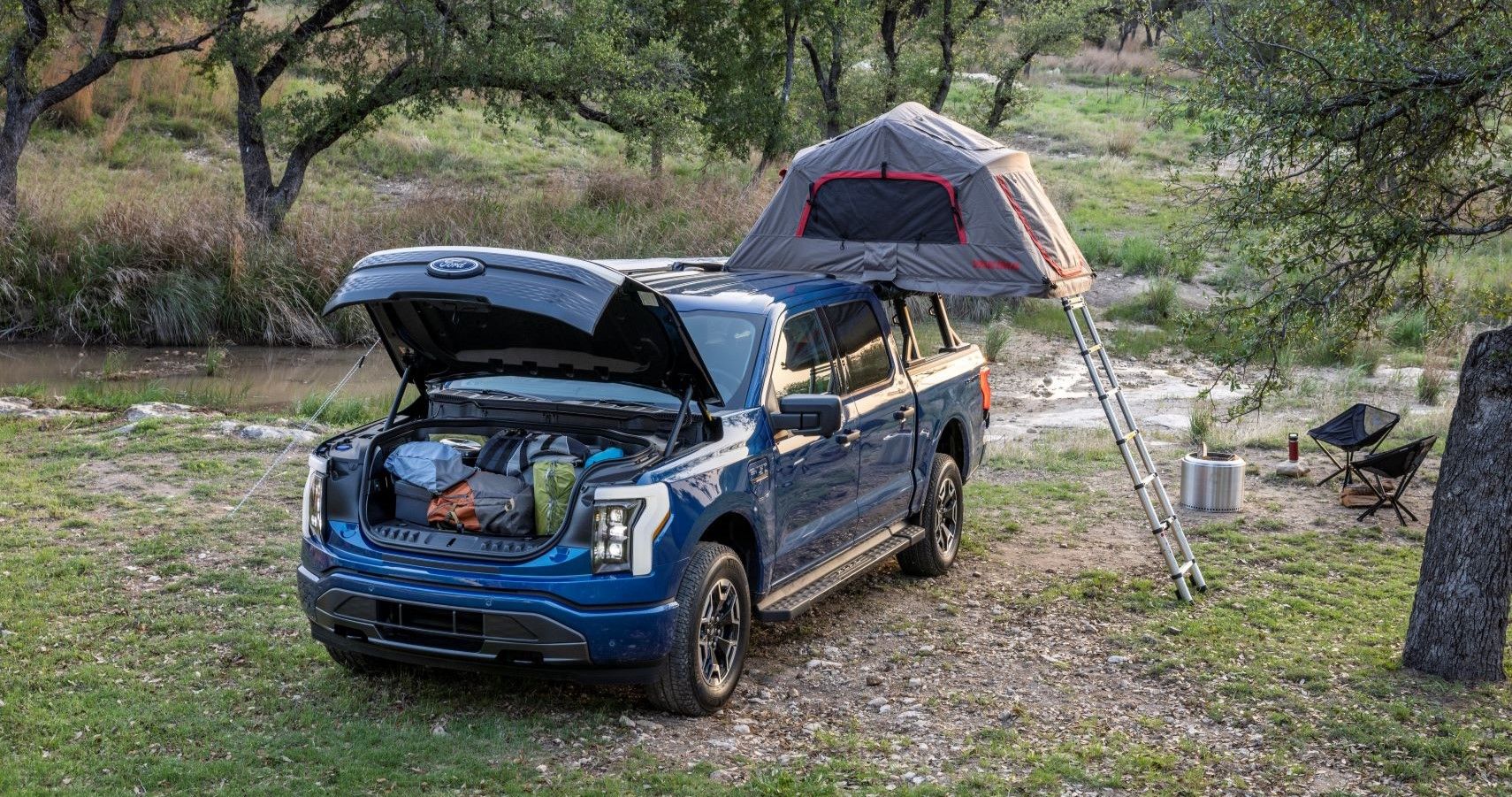 Van EV biru di hutan dengan tenda