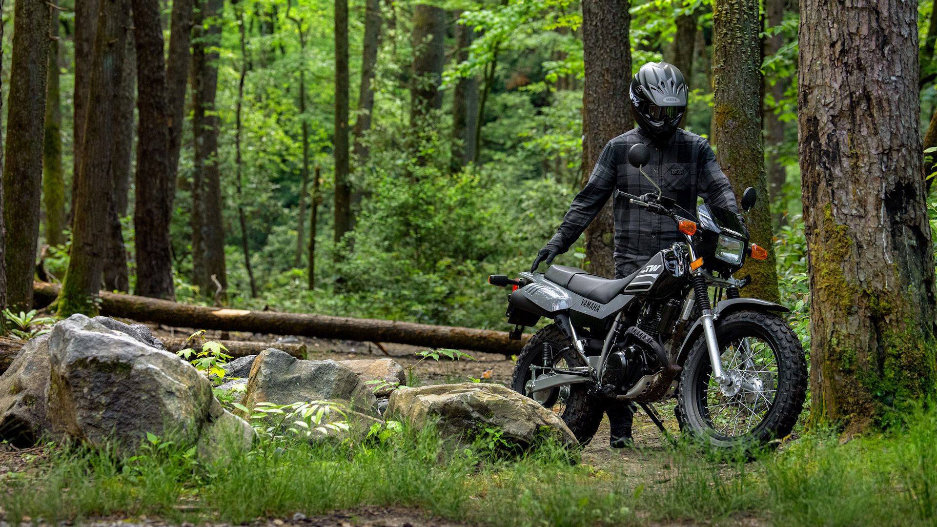 A rider standing by a gray 2023 Yamaha TW200