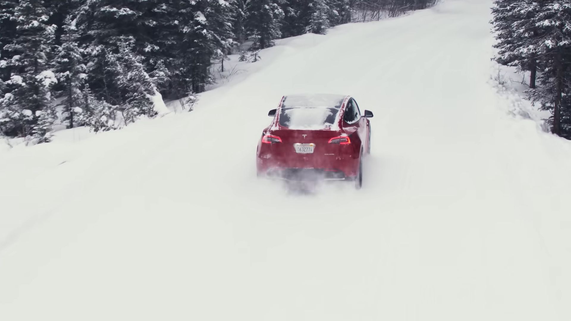 Bidikan aksi belakang Tesla Model Y yang sedang mengemudi di salju