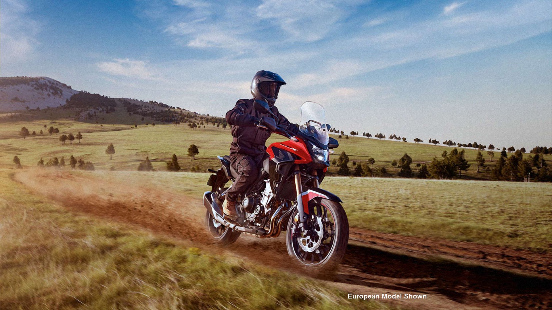 Red 2023 Honda CB500X cruising through a field