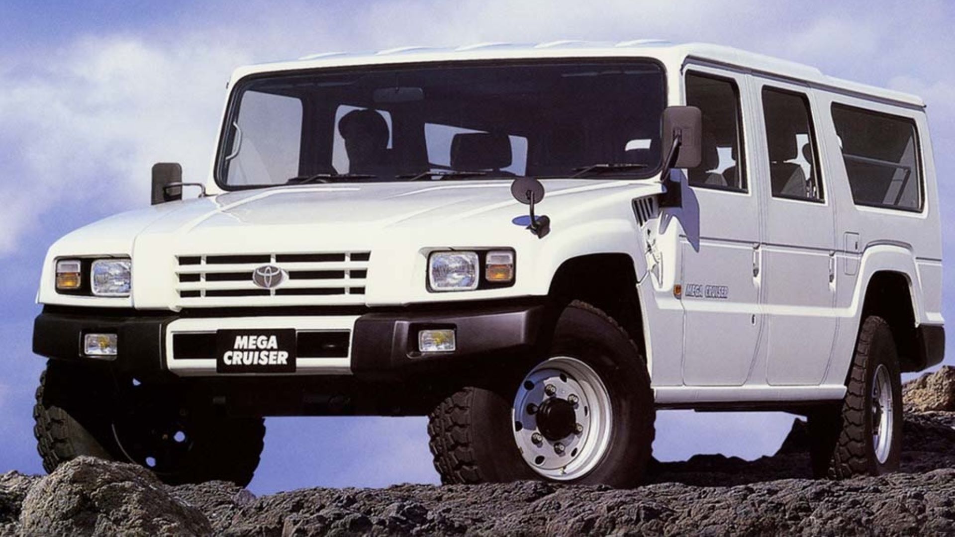 Front 3/4 shot of a white Toyota Mega Cruiser parked on rugged terrain