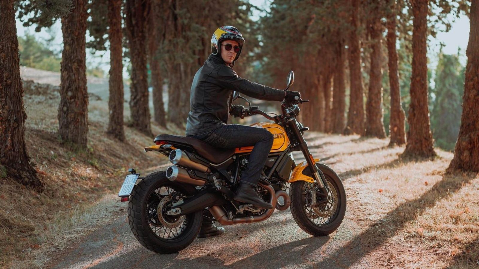 A rear 3/4 shot of a Ducati Scrambler 1100 Tribute Pro and its rider standing. 
