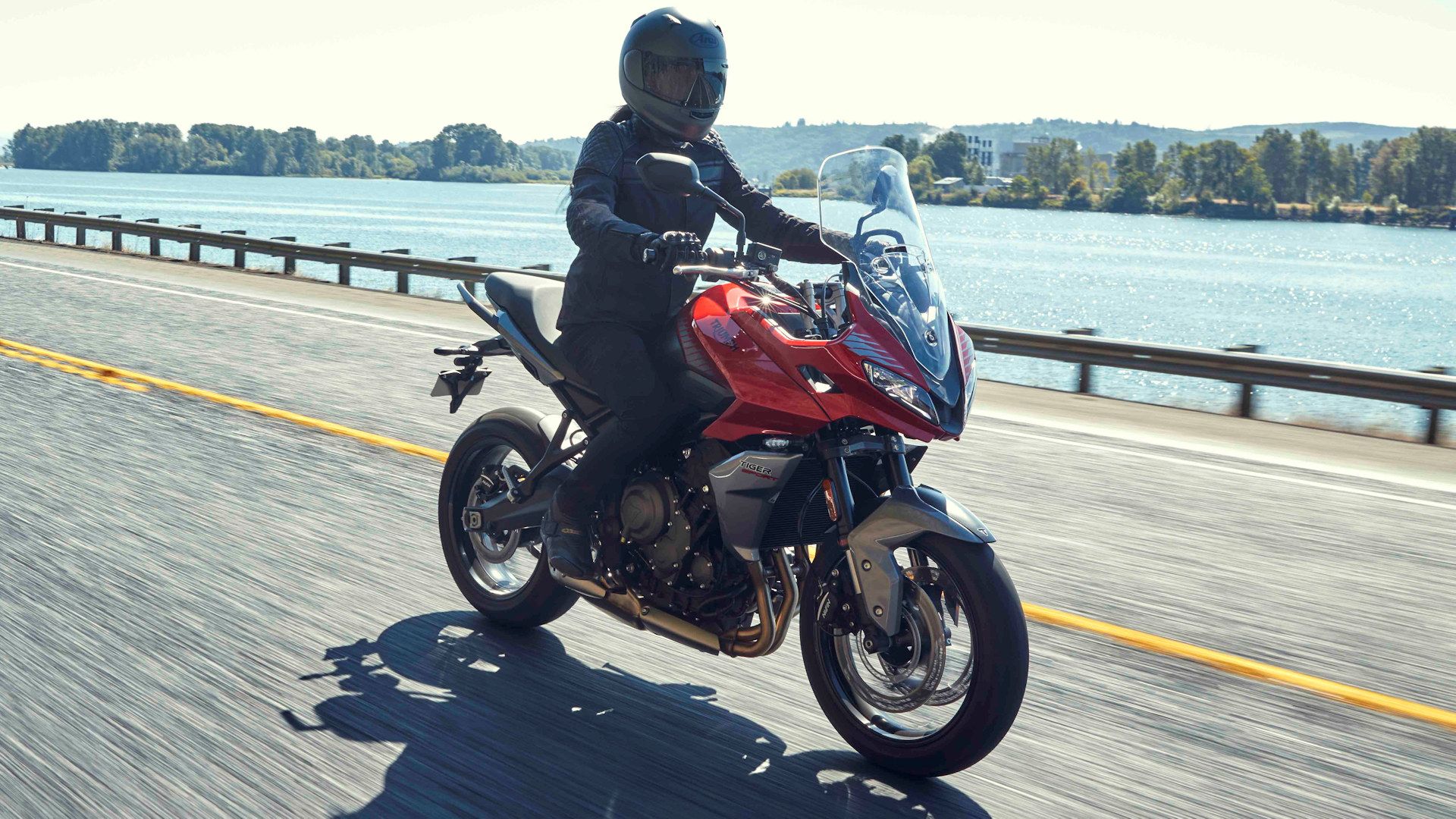 Red 2022 Triumph Tiger Sport 660 cruising over a bridge