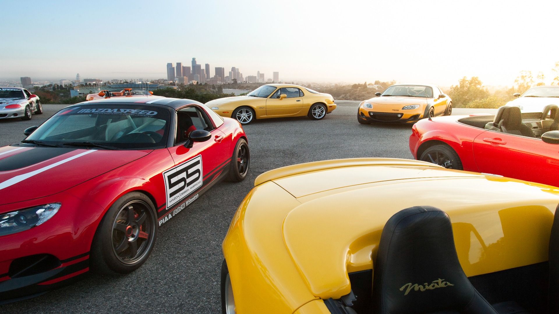 Close de dois miatas olhando para o encosto de cabeça do passageiro dianteiro e um Miata vermelho atrás