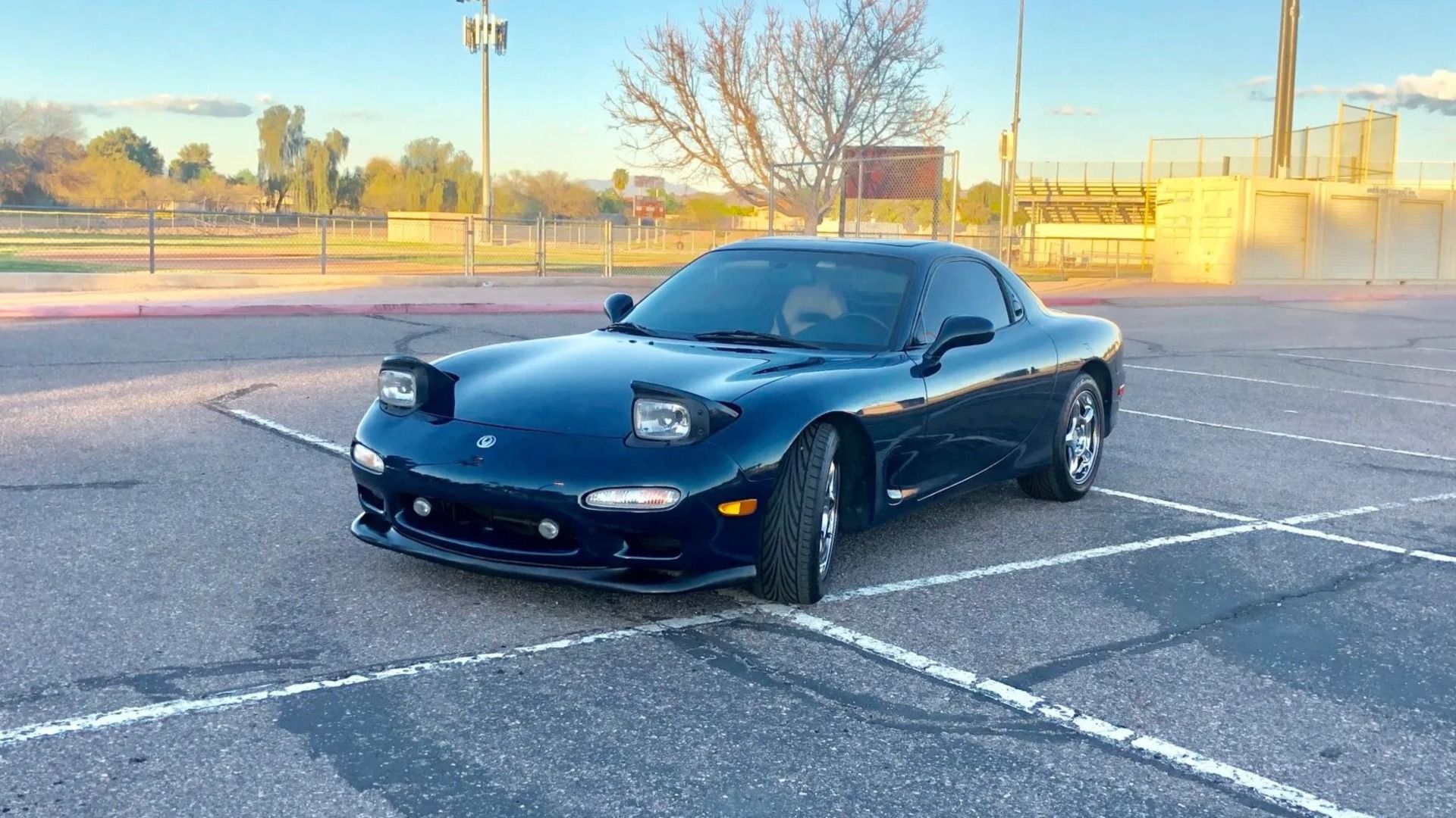 A blue-green 1994 Mazda RX-7 Touring psoing in the light of the setting sun.