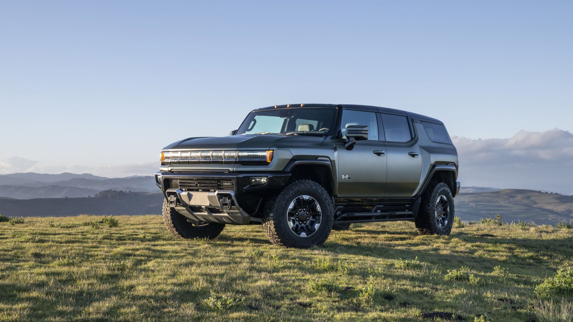 2024 GMC Hummer EV in green posing on grassy hill with hills in background