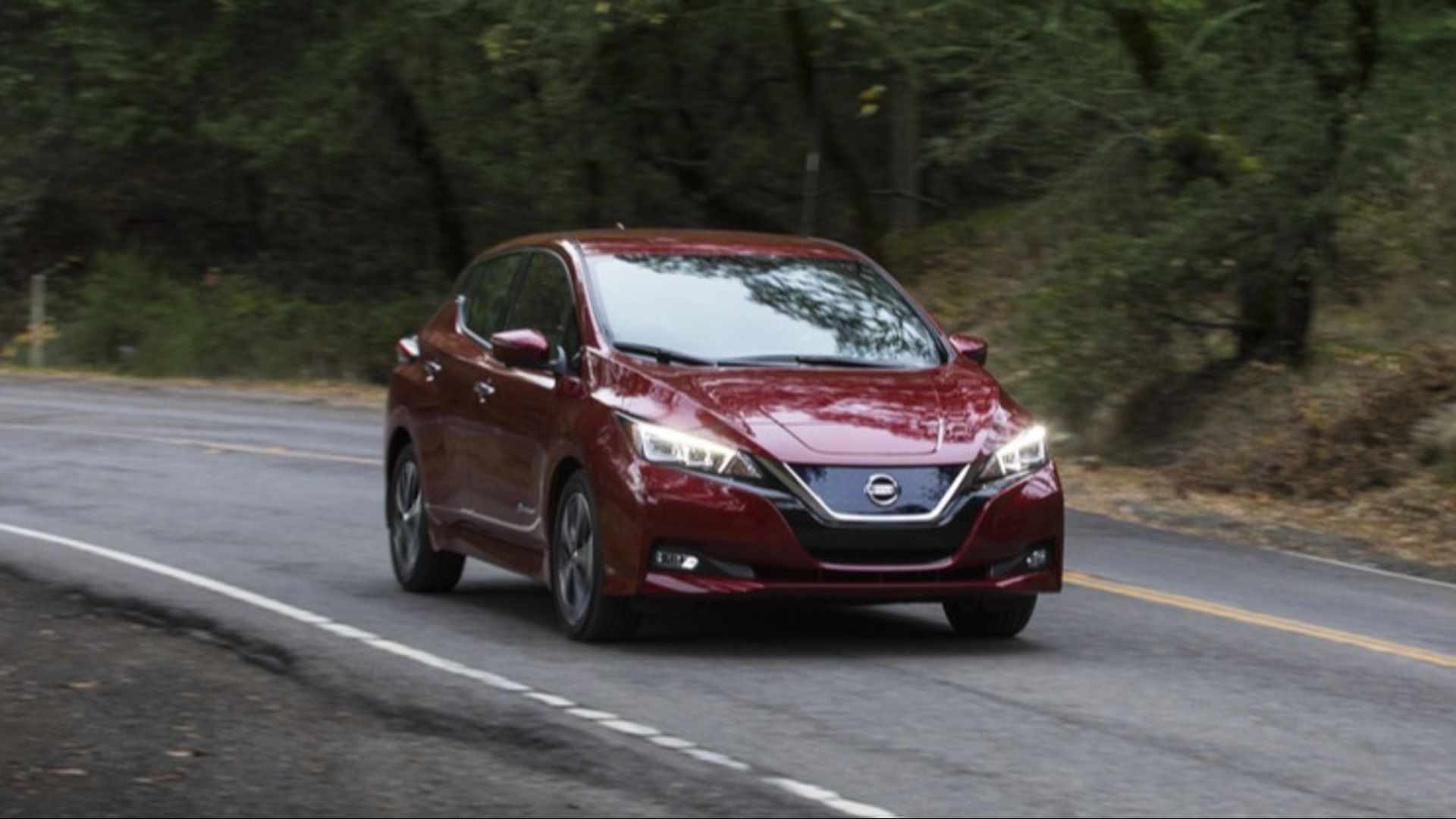 2018 Nissan Leaf in maroon out for a drive on a backroad past some woods.