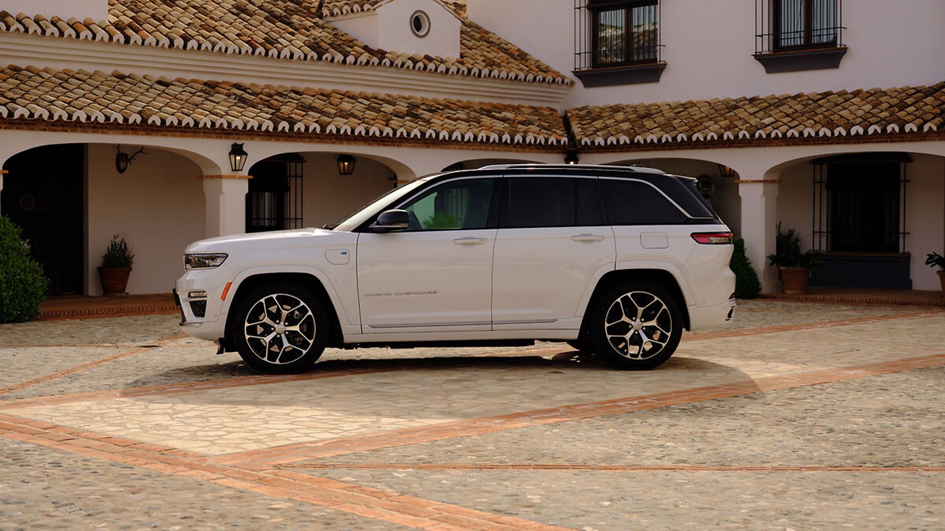 A white 2024 Jeep Grand Cherokee side left shot parked in front of a large house.