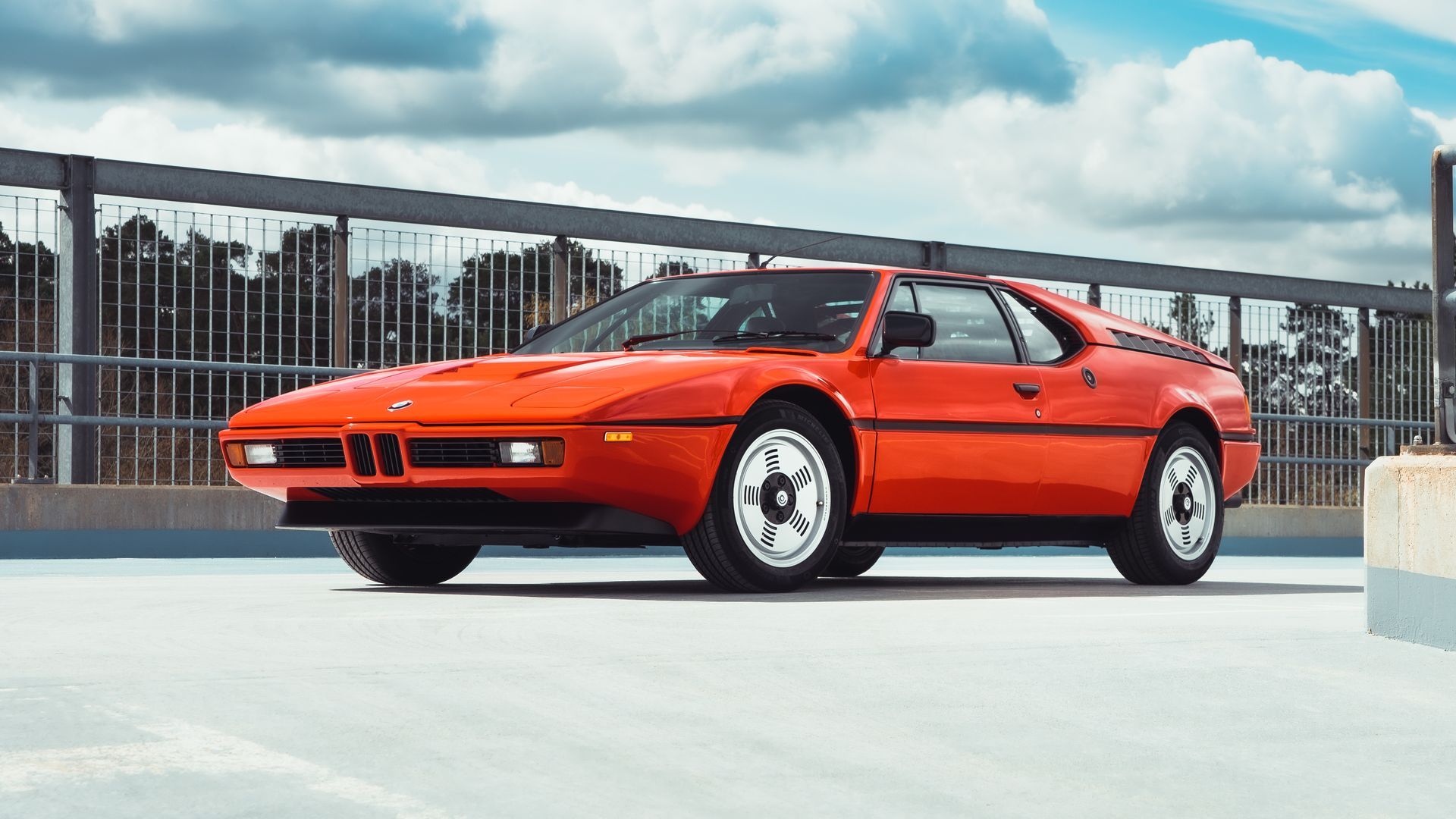 Supercarro BMW M1 laranja estacionado na frente 3/4 vista