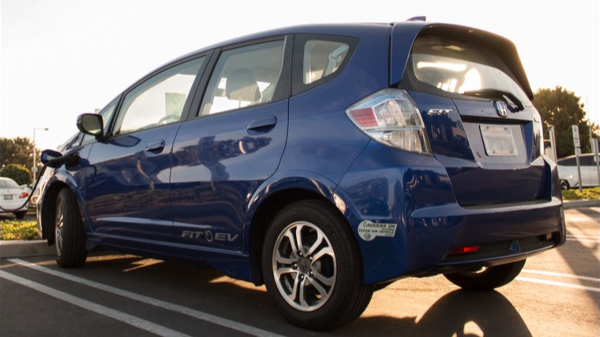 A dark blue Honda Fit EV parked at a recharging on a sunny day.