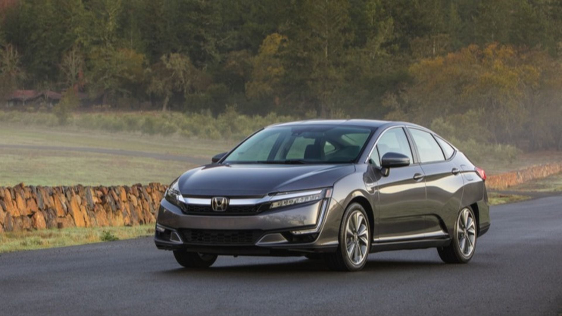 A metallic brown Honda Clarity EV driving on an early-morning misty country road