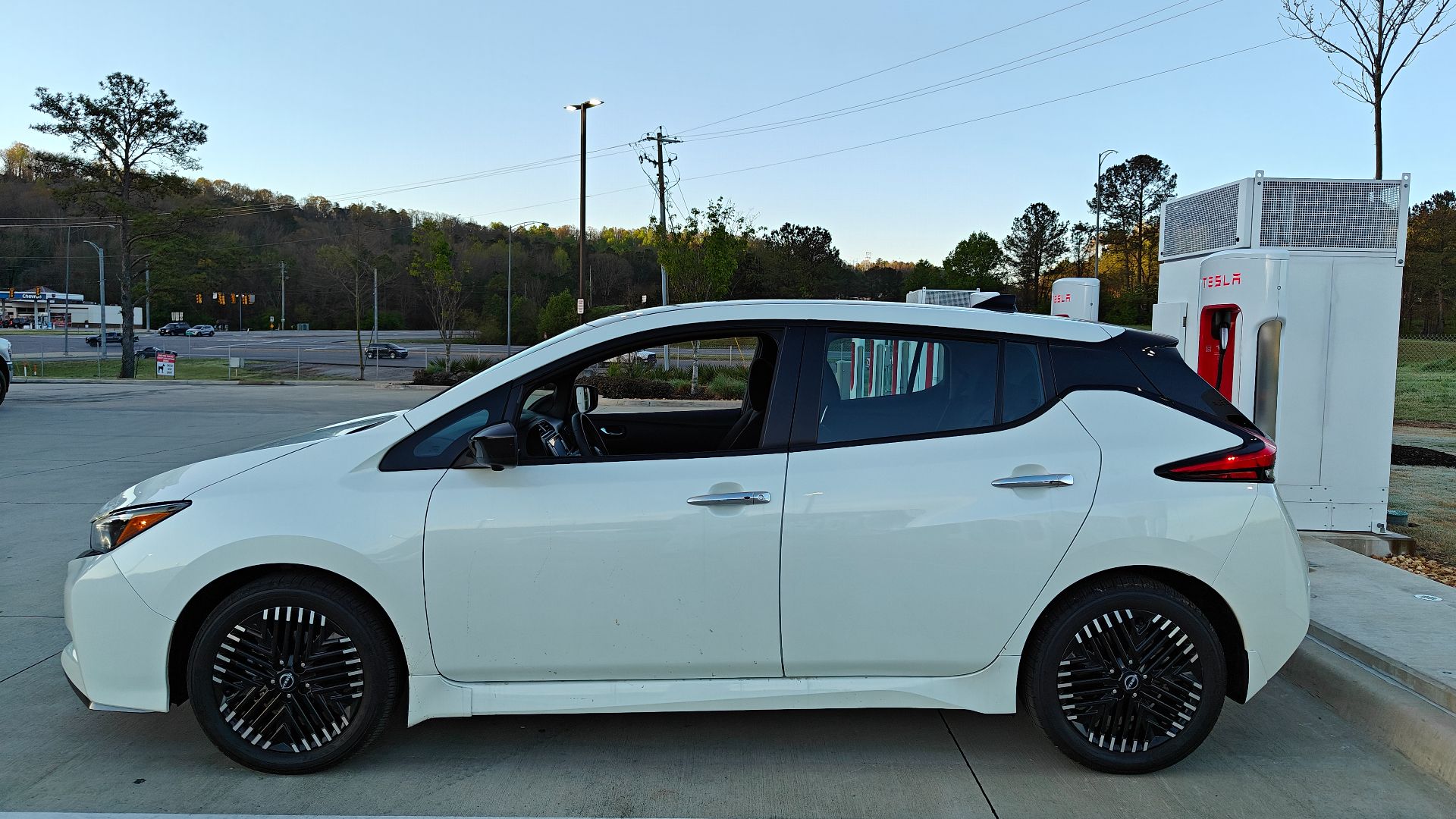 White 2024 Nissan Leaf next to Tesla Station