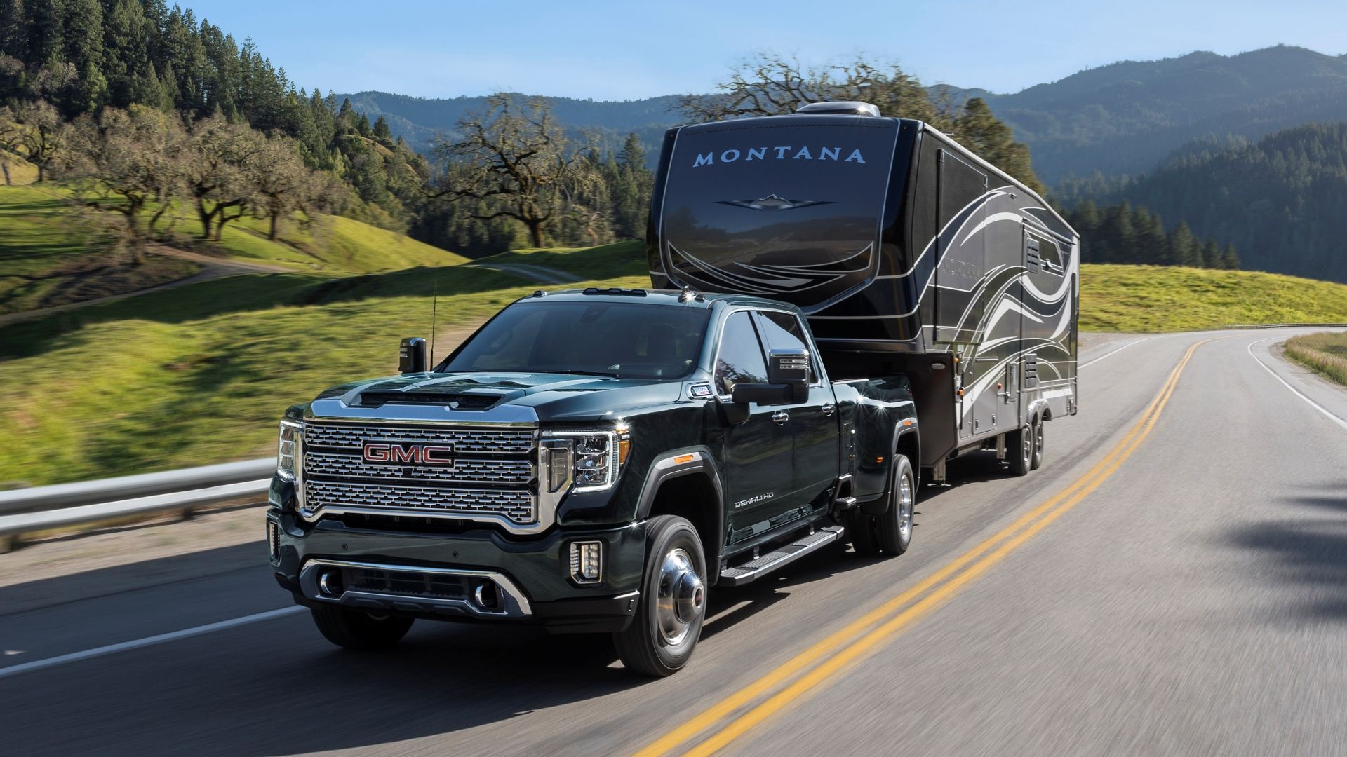 2023 GMC Sierra 3500 HD towing a trailer up a hill on the road. 