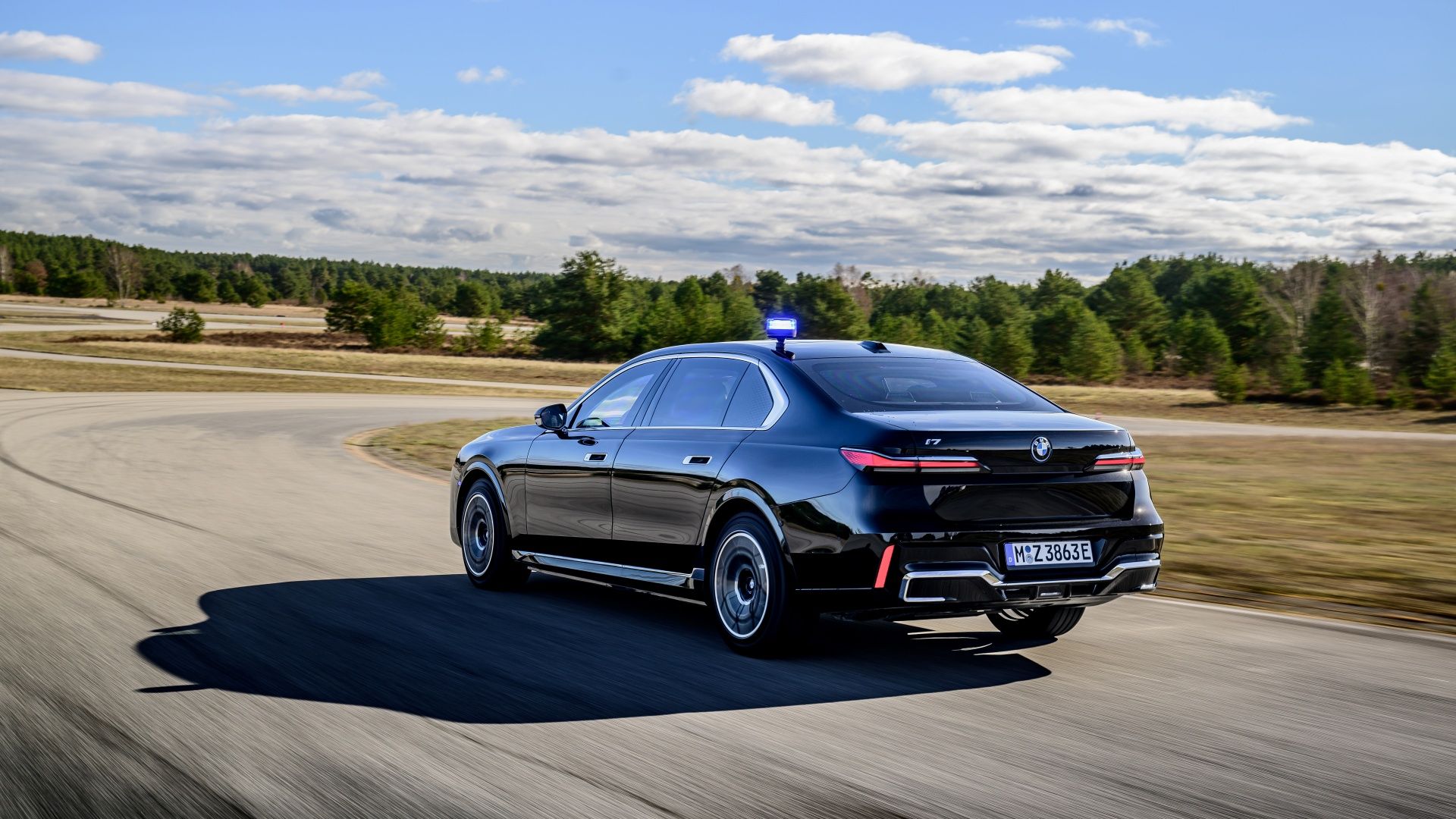 2024 BMW i7 xDrive rear driving on track with light on roof