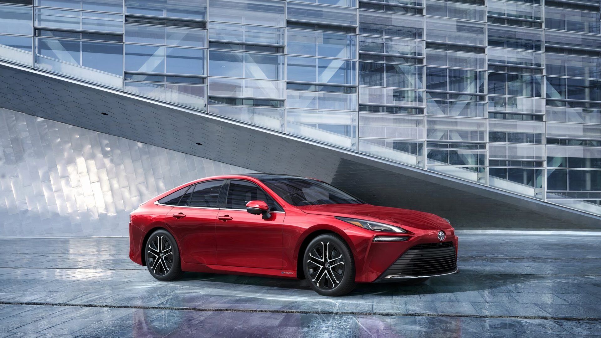 Toyota Mirai 2024 em vermelho posando em frente a um moderno edifício de escritórios