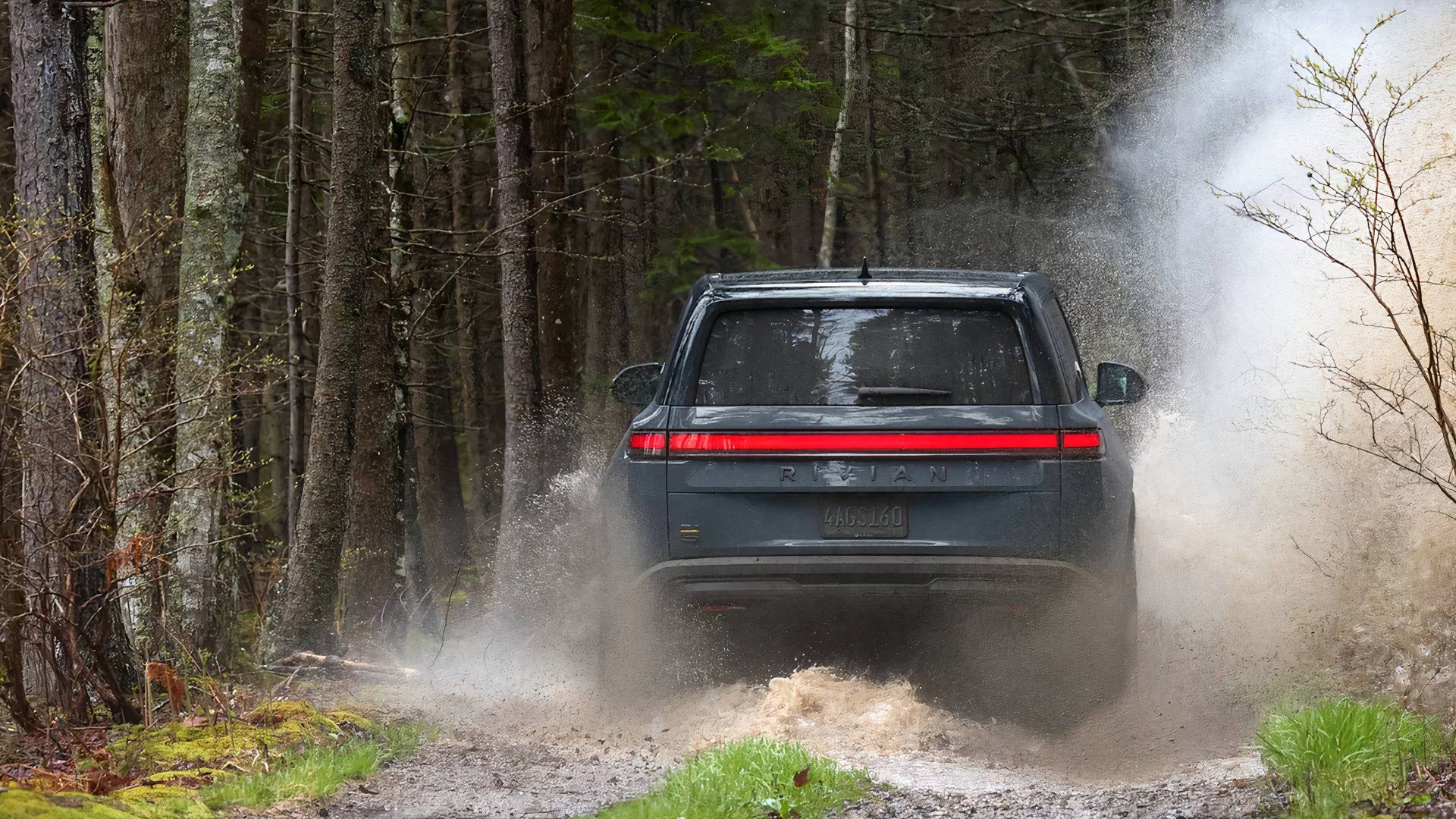 Um Rivian R1S 2025 azul está passando pela lama. 