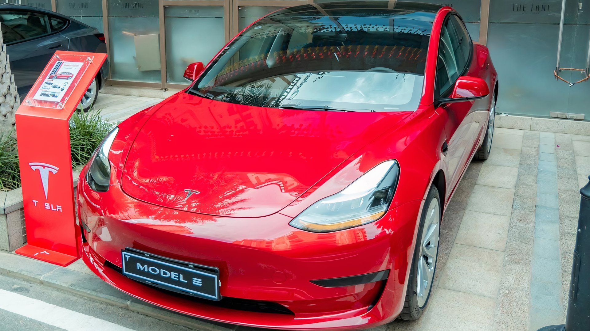 Tesla Model 3 vermelho 2017 estacionado em frente a uma concessionária