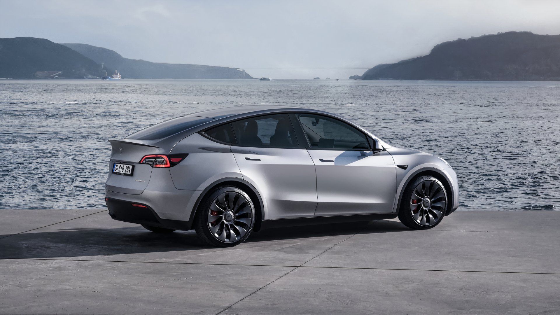 A gray Tesla Model Y is parked by the water. 