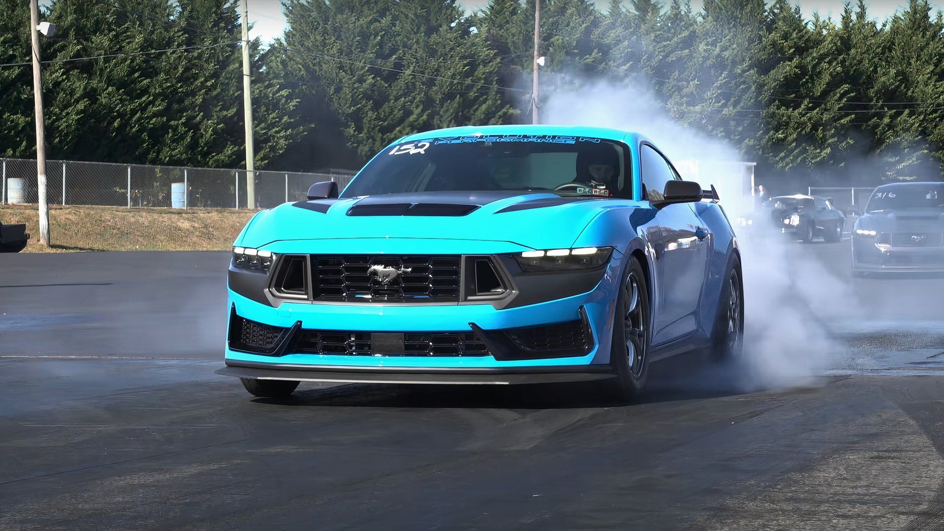 Vista frontal de três quartos de um Ford Mustang Dark Horse azul fazendo burnouts