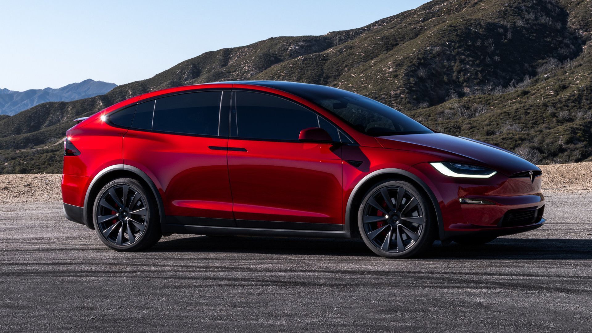 2024 Tesla Model X in red posing off-road in front of hills