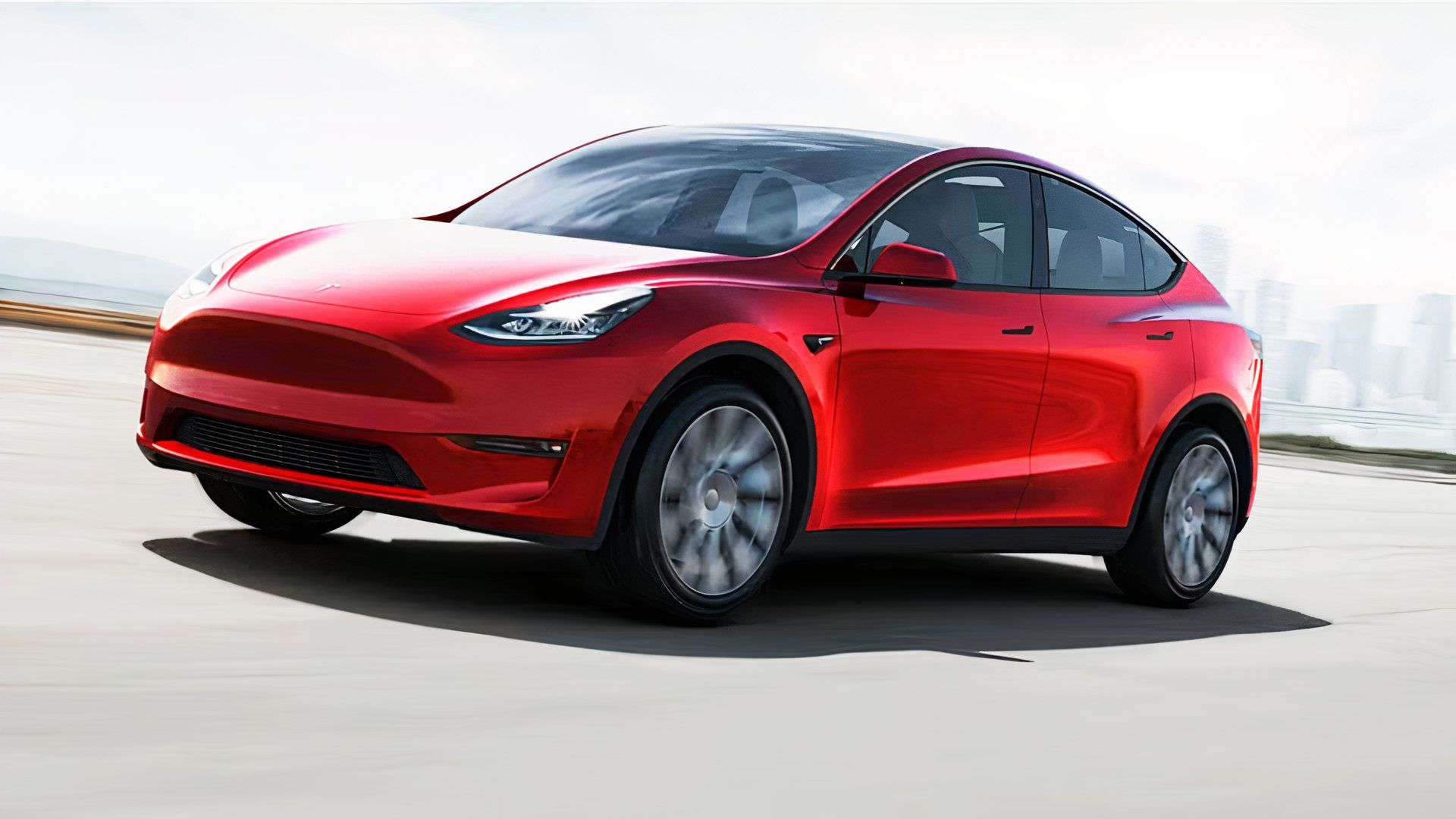 A red 2021 Tesla Model Y small electric SUV is driving on the road.