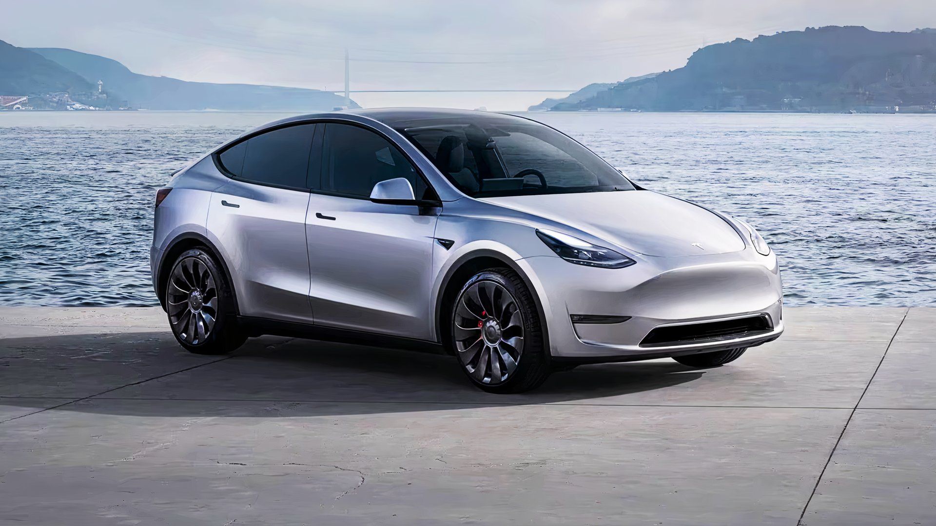 A gray 2021 Tesla Model Y small electric SUV is parked near water. 