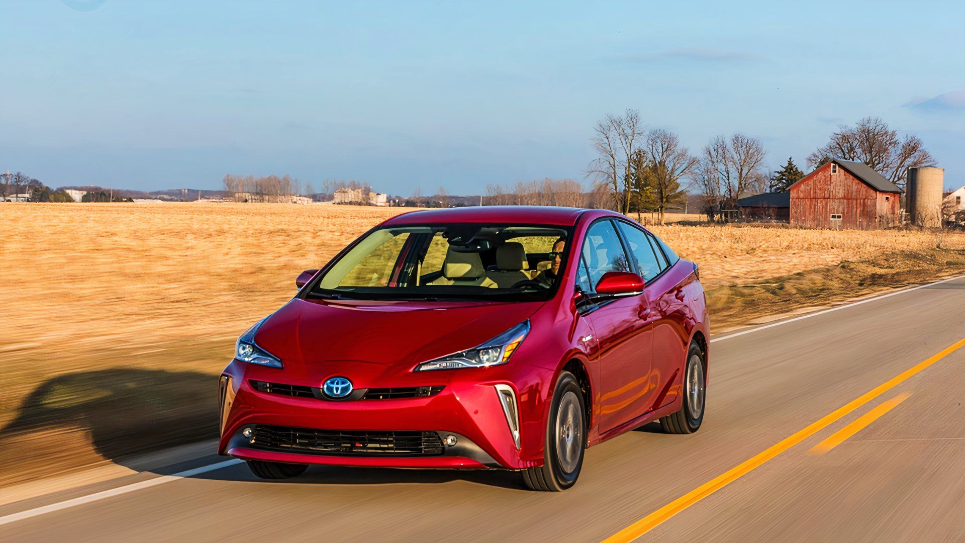 A red 2020 Toyota Prius hybrid car is driving on the road. 