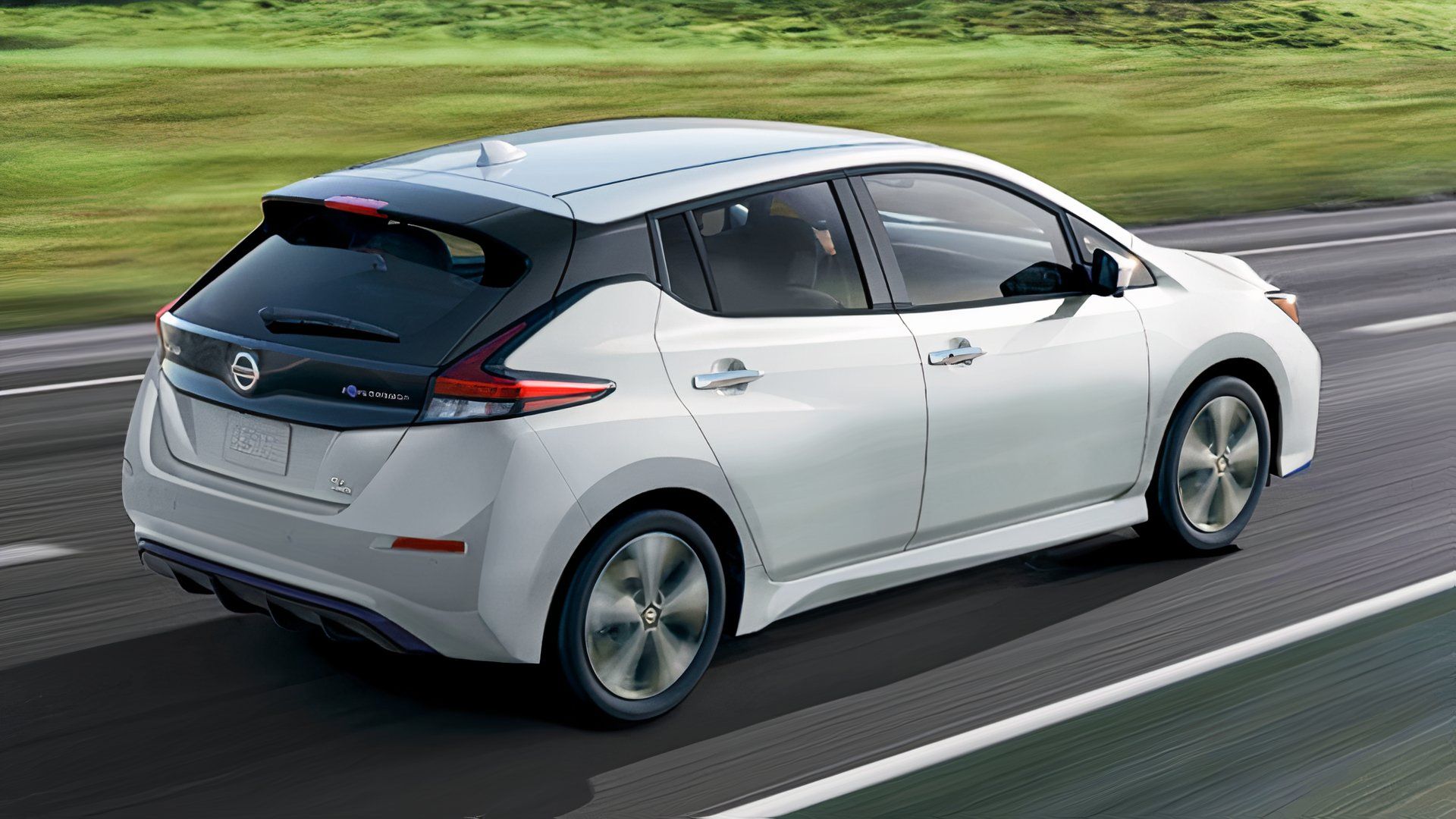 A white 2022 Nissan Leaf small electric car is driving. 