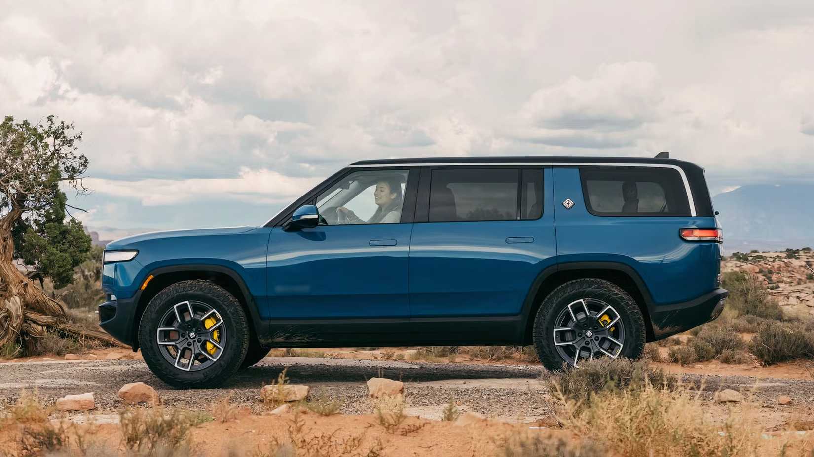 Side profile shot of a blue 2024 Rivian R1S with the badge blurred