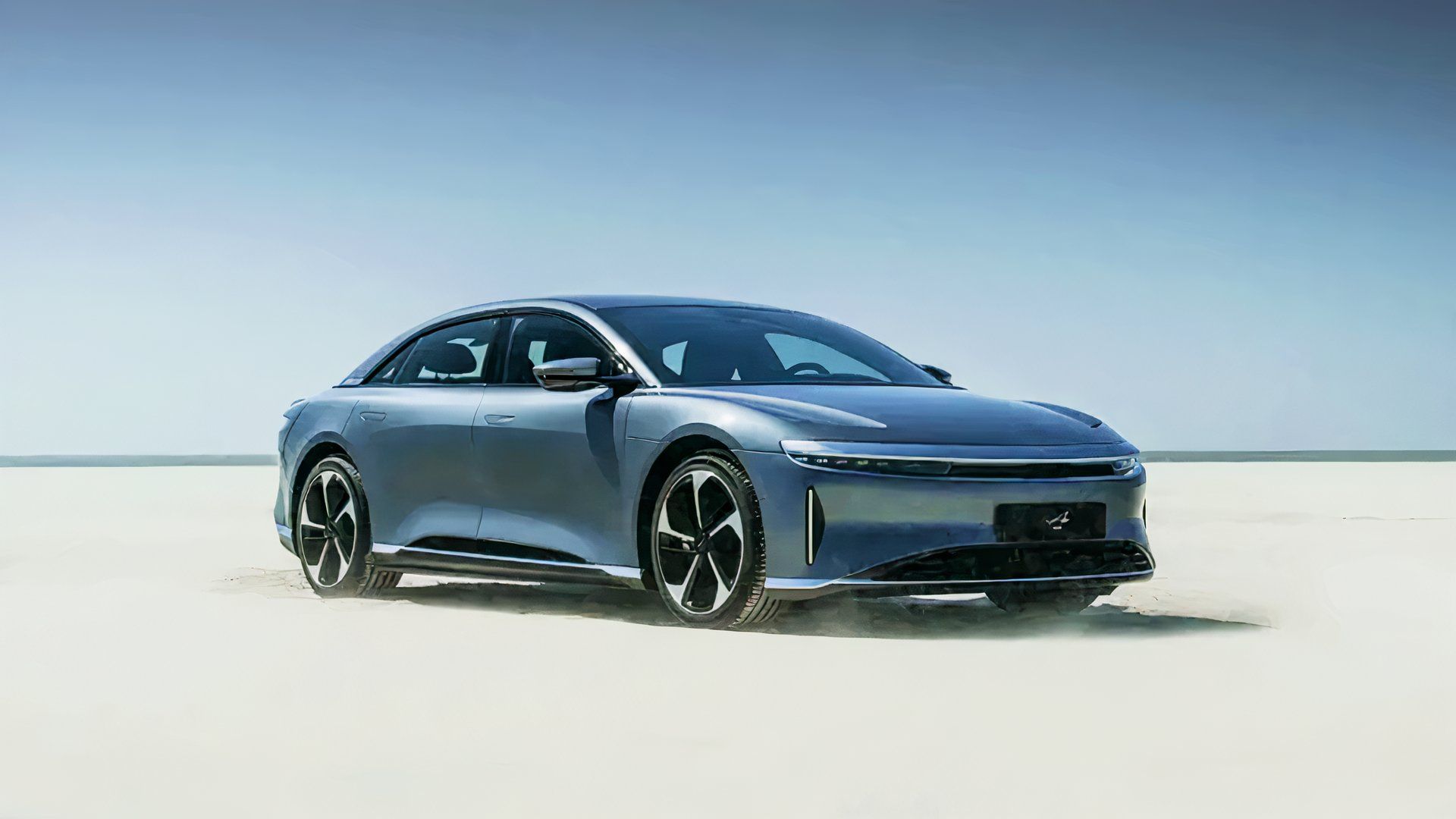 A gray Lucid Air is parked in sand. 