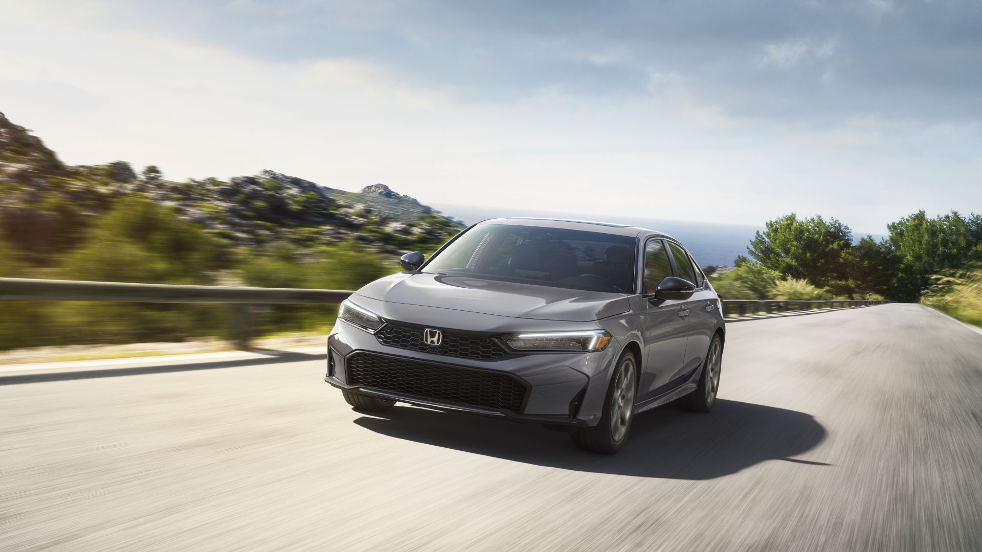 2025 Honda Civic Hatchback Sport Touring Hybrid Front Exterior Driving Down A Road