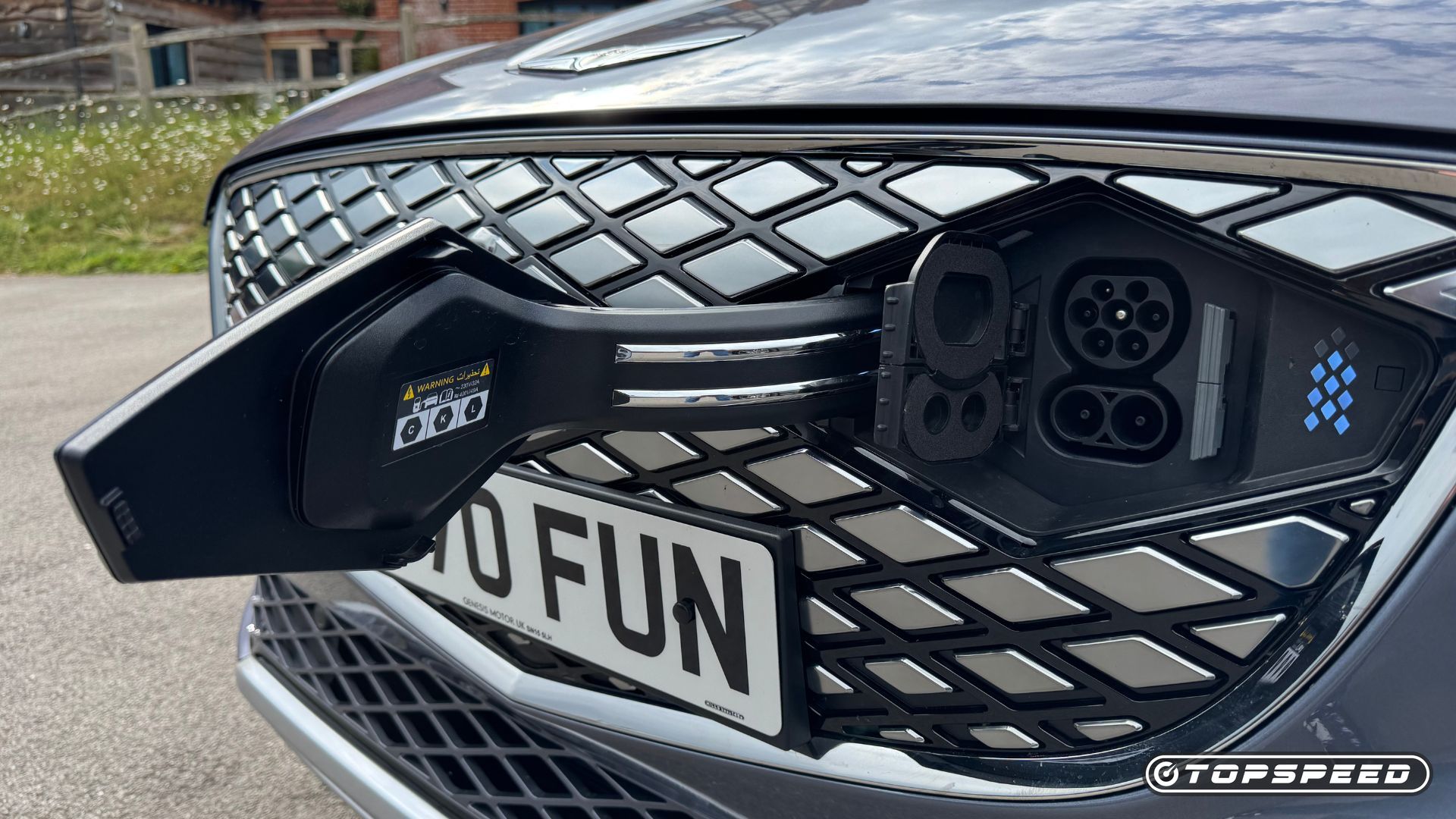 Close-up shot of the charging port in the front grille of a gray 2026 Genesis Electrified GV70.